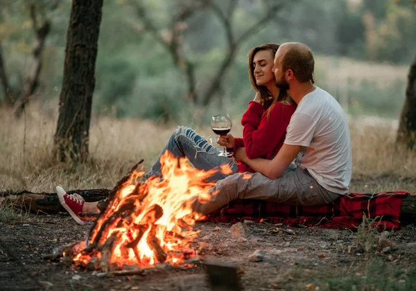 Verliebtes Paar sitzt und umarmt sich bei Picknick im Wald auf Lagerfeuer Flammenhintergrund. — Stockfoto