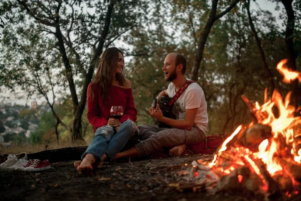 Jeune homme joue à la guitare et chante la chanson près de la fille sur fond de flamme de feu de joie . — Photo