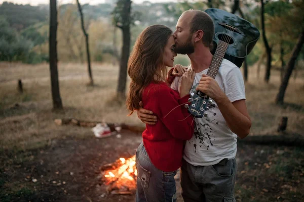 Ζευγάρι ερωτευμένων καθώς κοιτάζονται στέκεται με κιθάρα, αγκαλιές και φιλιά φόντο φωτιά φλόγα. — Φωτογραφία Αρχείου