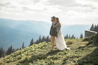 Yeni evliler stand, gülümseme ve dağlar kucaklama.