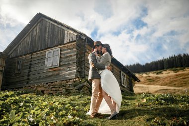 Yeni evliler ve stand Mount eski ahşap kulübe arka plan üzerinde sarılmak