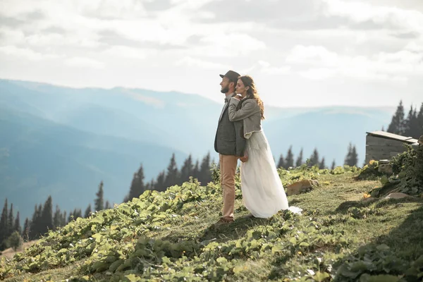 Les jeunes mariés se tiennent debout, sourient et se câlinent dans les montagnes . — Photo