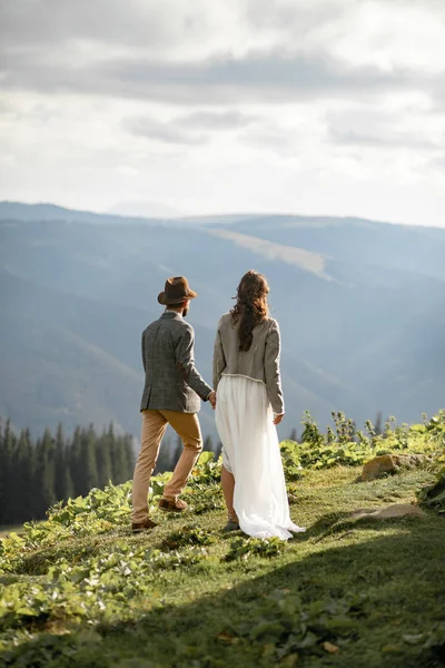 Les jeunes mariés marchent et se tiennent la main dans les montagnes . — Photo