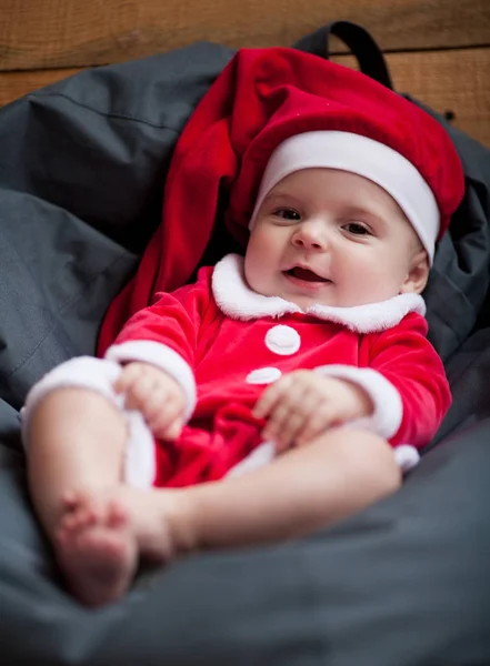 Meisje van de baby in Santa Claus kostuum zit onder het kussen en glimlacht. — Stockfoto