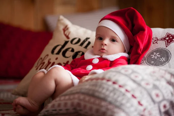 Bebé niña en traje de Santa Claus se sienta entre almohadas . —  Fotos de Stock