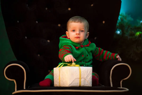 Menino senta-se em poltrona com caixa de presente de Natal . — Fotografia de Stock