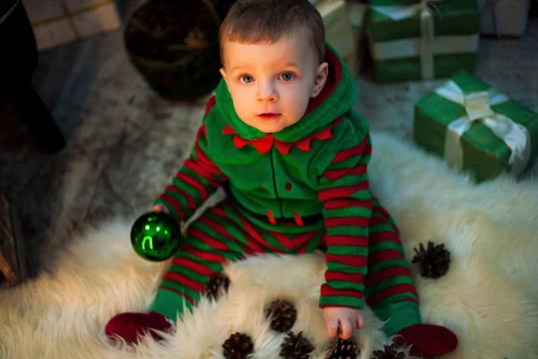 Little boy holds Christmas ball in hand, sits and plays by pine cones. — Stock Photo, Image