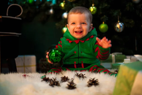 Feliz niño sostiene la bola de Navidad en la mano, se sienta y sonríe . —  Fotos de Stock