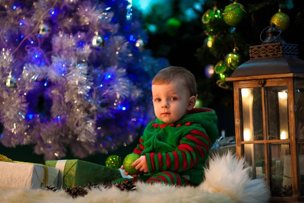 小さな男の子クリスマス ボールを手で保持しているし、クリスマス ツリーの近くに座っています。. — ストック写真