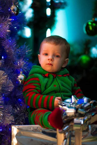 Niño pequeño se sienta cerca del árbol de Navidad y cajas de regalo . —  Fotos de Stock