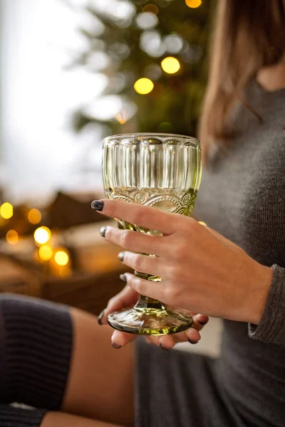 El primer plano de la copa del vino en las manos de la mujer joven sobre el fondo de las luces de fiesta . — Foto de Stock