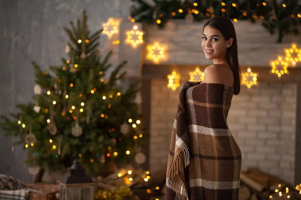 Genç kadın ekose içinde sarılı mutlu Noel ağacı reklam ışıklar arka plan üzerinde duruyor. Sol kopya alanı. — Stok fotoğraf