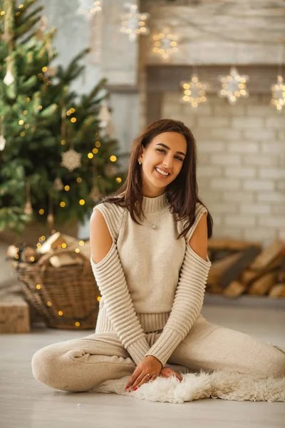 年轻的女人微笑着坐在圣诞树的背景上. — 图库照片