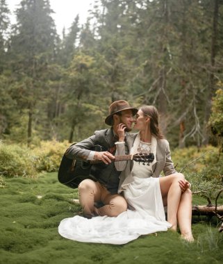 Gelin ve damat gitar ile yosun orman arasında oturmak. 