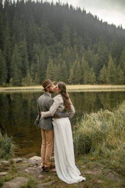 Gelin ve damat stand ve orman göl kenarında kucaklamak.