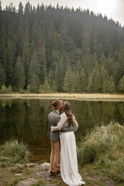 Gelin ve damat stand ve orman göl kenarında kucaklamak.