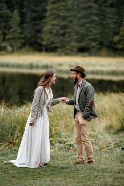 Gelin ve damat ayakta, tutuşup vardır ve orman göl kenarında gülmek.