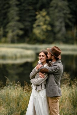 Gelin ve damat gülümseyerek ayağa ve orman göl kenarında kucaklamak. 