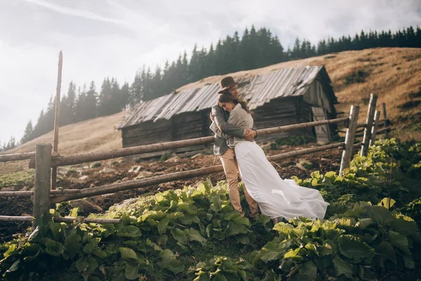 Yeni evliler standı, gülümseme ve eski ahşap kulübe ve çit arka hug.
