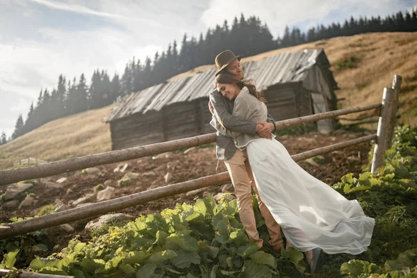 Yeni evliler standı, gülümseme ve eski ahşap kulübe ve Karpat Dağları'nda çit arka hug.