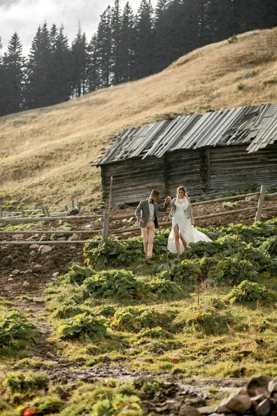 Gelin ve damat eski ahşap kulübe ve Karpat Dağları'nda çit arka plan üzerinde yürümek.