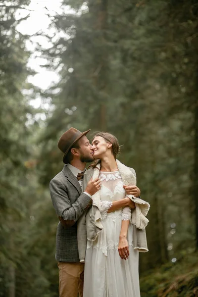 Bride and groom stand in forest and embrace. — Stock Photo, Image