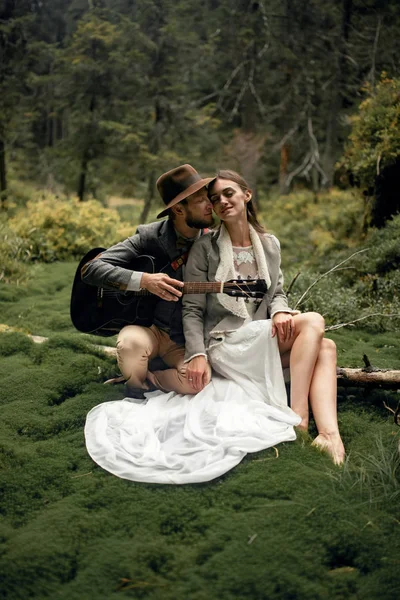 Gelin ve damat gitar ile yosun orman arasında oturmak. 