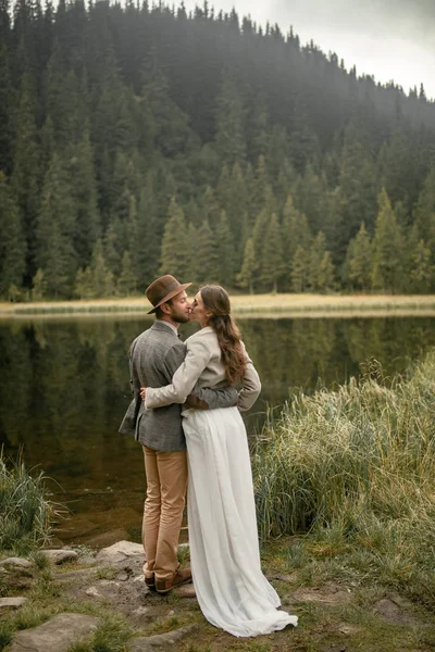 Gelin ve damat stand ve orman göl kenarında kucaklamak.