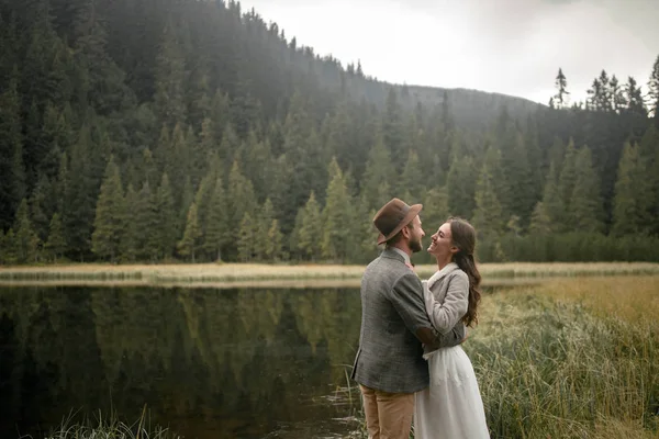 Novia y novio de pie, abrazar y reír cerca del lago del bosque . — Foto de Stock