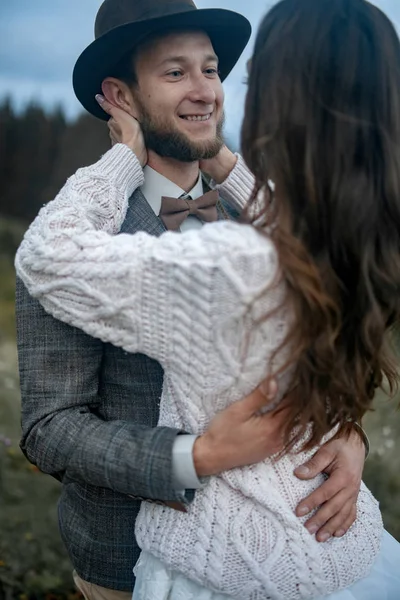 Bruid en bruidegom staan, glimlach en knuffel op achtergrond van bergen. — Stockfoto