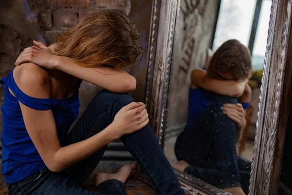Mulher vítima de violência doméstica e abuso chora e se senta no chão perto do espelho com hematomas e feridas em seu corpo . — Fotografia de Stock