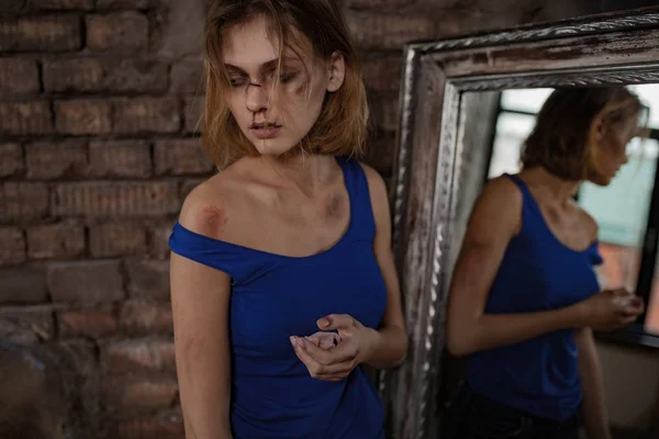 Сумна жінка-жертва домашнього насильства і жорстокого поводження стоїть біля дзеркала з синцями і ранами на її обличчі і тілі . — стокове фото