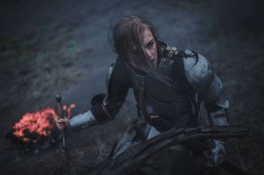 Jeanne d'Arc zırh ve onun elinde kılıçla görüntüsünü kız ateş ve duman arka planı diz çöker..