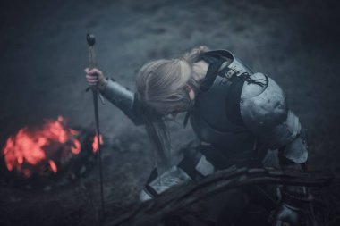 Jeanne d'Arc zırh ve onun elinde kılıçla görüntüsünü kız ateş ve duman arka planı diz çöker..