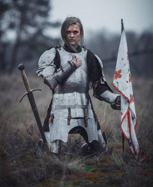 Jeanne d'Arc zırh görüntüsünü kız ellerini ve çayır ateşe bayrağı ile diz çöker.