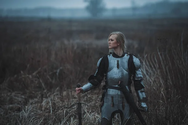 Chica en la imagen de Jeanne d 'Arc en armadura y con la espada en sus manos se encuentra en el prado. Primer plano. . — Foto de Stock