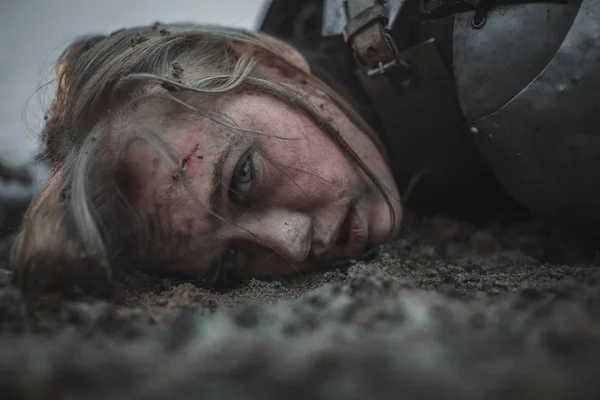 Fille avec des blessures sur le visage à l'image de Jeanne d'Arc gît dans la boue en armure . — Photo