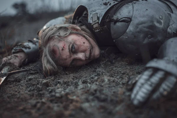 Девушка в образе Жанны д 'Арк в доспехах лежит в грязи с мечом в руках . — стоковое фото