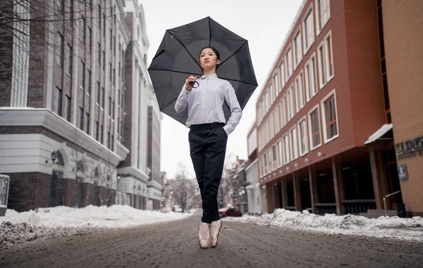 Bailarina con paraguas en sus manos está de pie en la calle de la ciudad contra la nieve y los edificios de fondo . —  Fotos de Stock