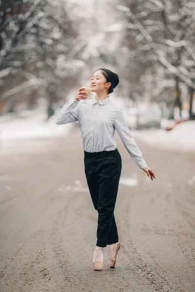 Bailarina con un vaso de raf de café caliente en sus manos está de pie en la calle de la ciudad contra la nieve y el fondo de invierno . —  Fotos de Stock