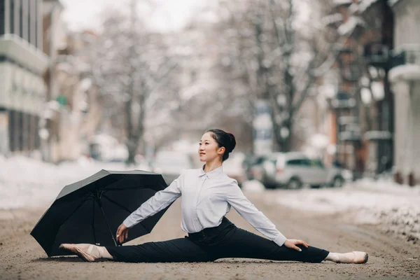 Bailarina con paraguas está sentada en cordel de pose gimnástica en medio de la calle de la ciudad . —  Fotos de Stock