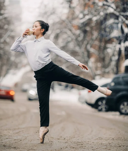 Bailarina con un vaso de café caliente en sus manos está de pie en la calle de la ciudad contra la nieve y el fondo de invierno . —  Fotos de Stock