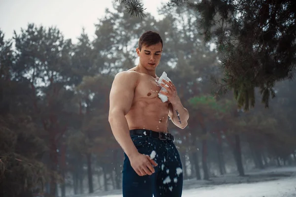Young bodybuilder with bare torso wipes his body by snow in forest in winter. — Stock Photo, Image