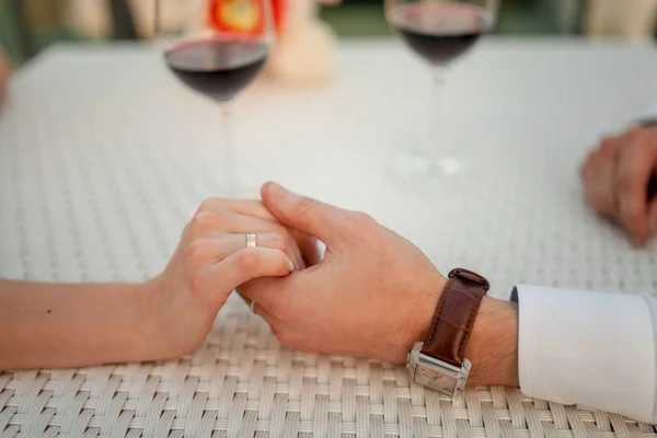 El hombre sostiene la mano de la mujer en la cafetería en el fondo de las gafas de vino. Primer plano. . — Foto de Stock