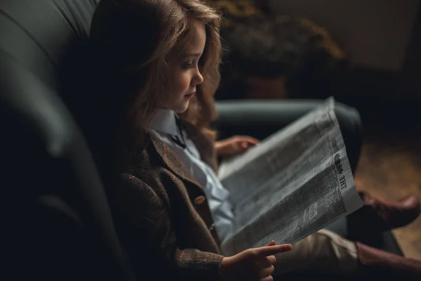 Κορίτσι παιδί κάθεται στην πολυθρόνα και διαβάζει Εφημερίδα. — Φωτογραφία Αρχείου
