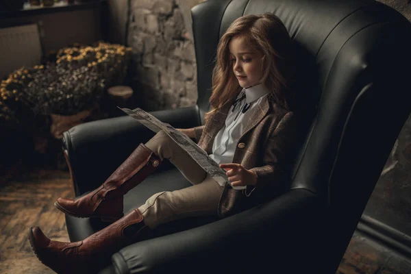 Παιδί κορίτσι στην εικόνα του Σέρλοκ Χολμς κάθεται στην πολυθρόνα και διαβάζει εφημερίδα σε φόντο παλιό εσωτερικό. — Φωτογραφία Αρχείου
