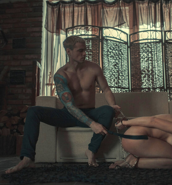 Man tied the woman's hands and legs by chain and spanks her by whip during a love game in dark room.