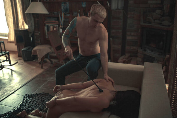 Man tied the woman's hands and legs by chain and spanks her by whip during a love game in dark room.