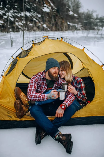 Jovem casal senta-se na tenda e bebe chá quente durante a caminhada de inverno . — Fotografia de Stock