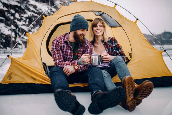 Jeune couple assis dans une tente, sourit et boit du thé chaud pendant le wint — Photo